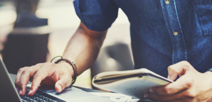 man with notebook working on laptop computer